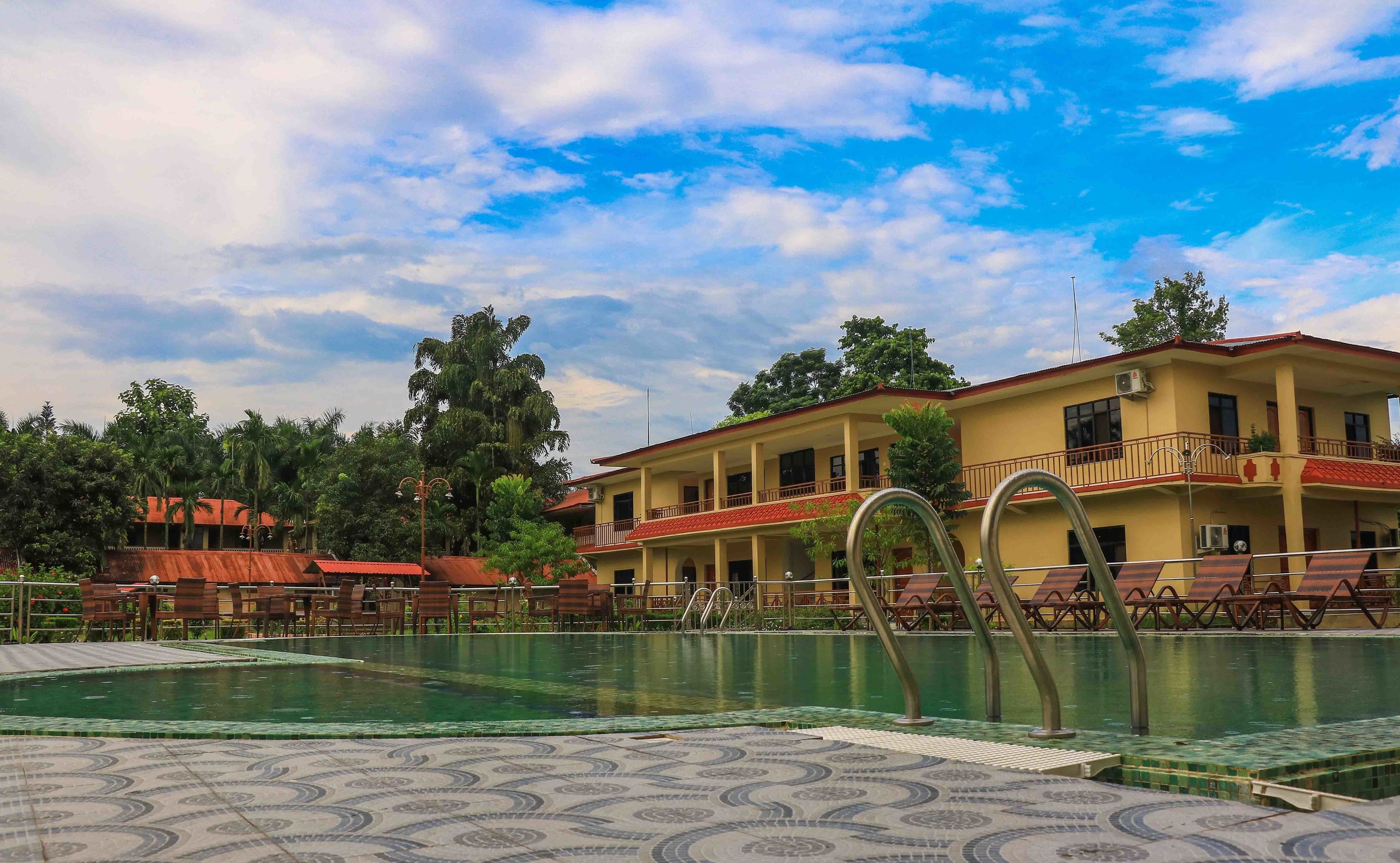 A hotel with a swimming pool, outdoor seating, and a two-story building with balconies.