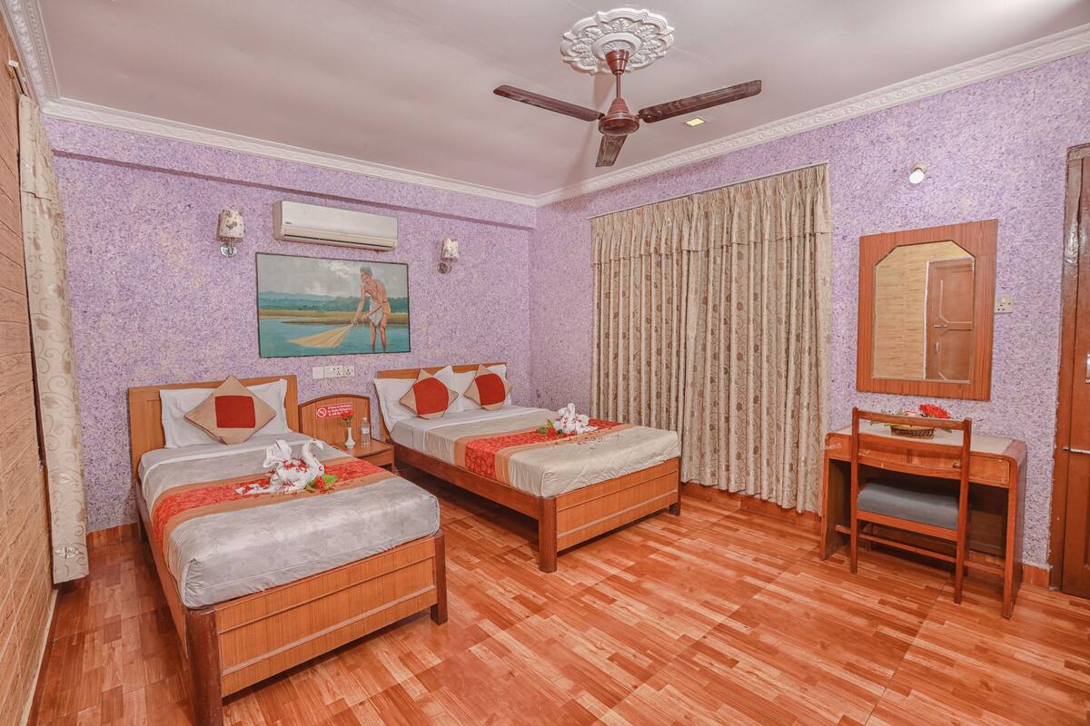 A hotel room with two wooden beds, a ceiling fan, a desk, and a mirror.