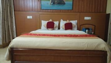 A hotel room with a wooden headboard, a painting of an elephant, a bed with red and beige pillows, and a nightstand with water bottles.