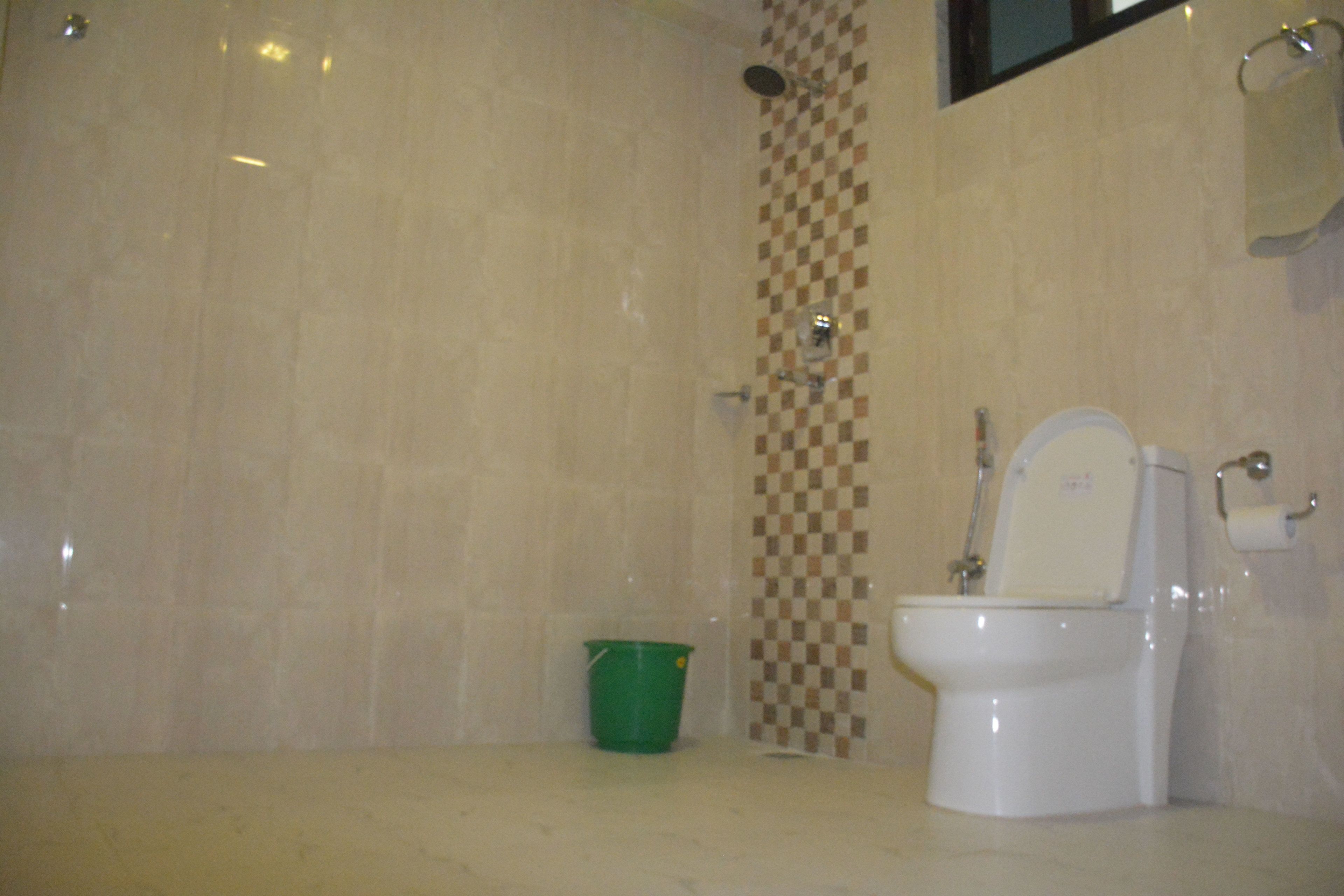 Un baño con inodoro, un balde verde y una ducha.