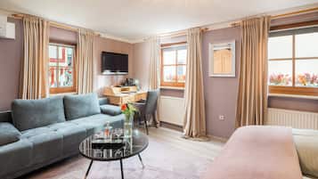 Ein modernes Wohnzimmer mit grauem Sofa, rundem Couchtisch mit Vase, Bett und Schreibtisch mit Stuhl.