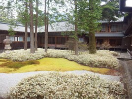 A traditional Japanese garden with a koi pond, surrounded by stone lanterns and a wooden building with sliding doors.