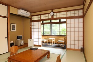 A traditional Japanese room with tatami flooring, a wooden table, a TV, a small refrigerator, and a view through shoji screens to the outside.