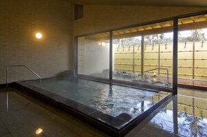 A hot tub with a glass enclosure, a metal railing, and a view of a bamboo fence outside.
