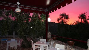 An outdoor dining area with tables and chairs, a stone wall, and a view of the sunset.