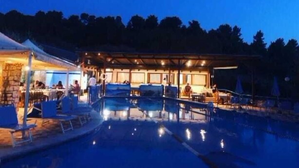 A nighttime outdoor pool area with a covered seating area and a stone structure.