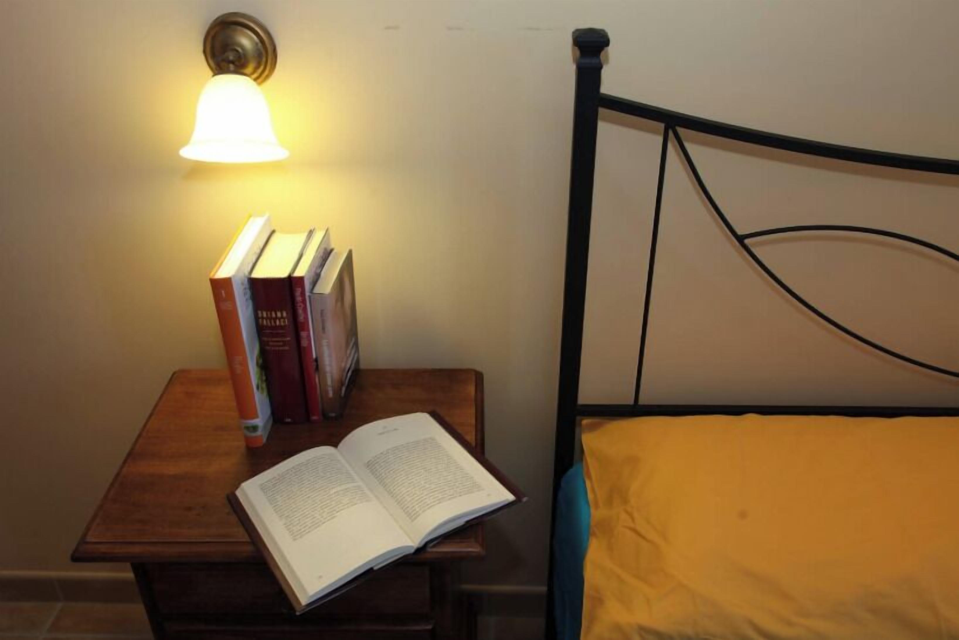 Una cama con cabecera, una mesita de noche con lámpara y un libro sobre la mesa.