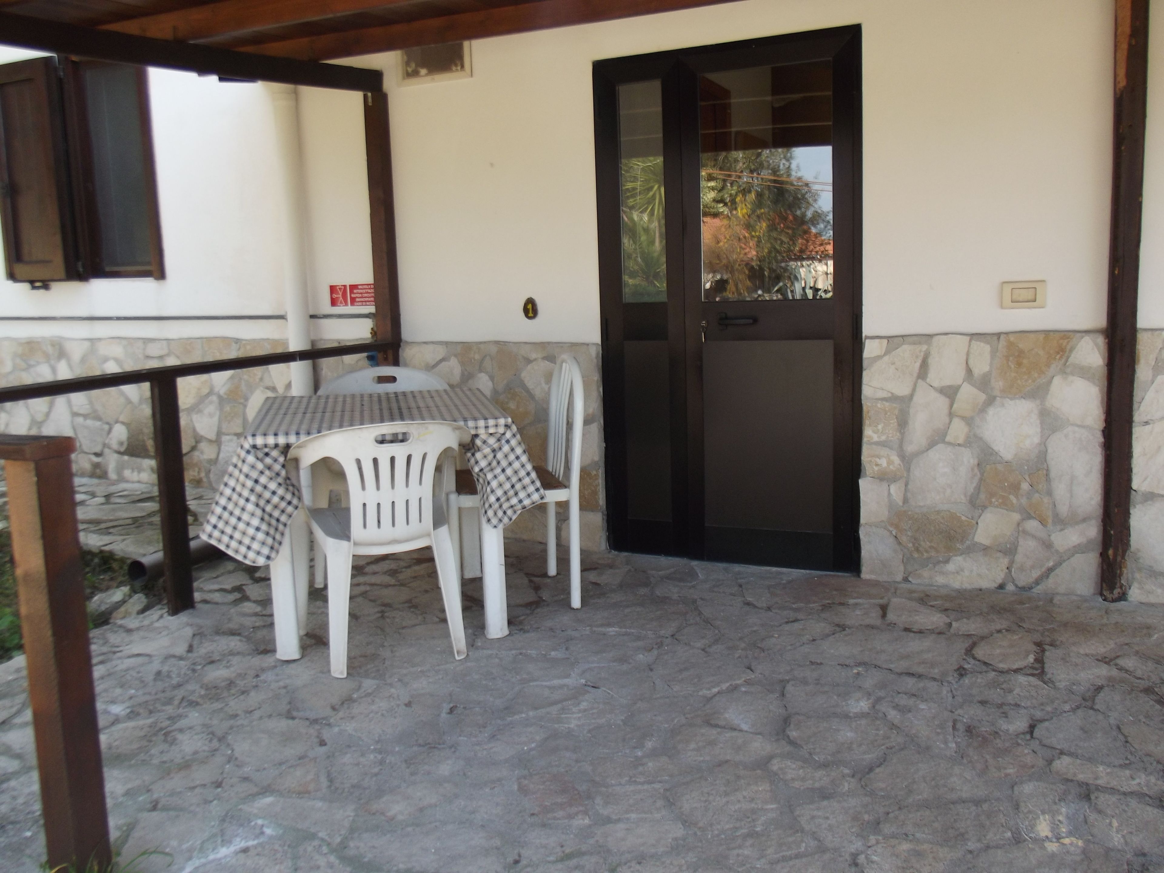 A patio with a table and chairs, a stone wall, and a door.