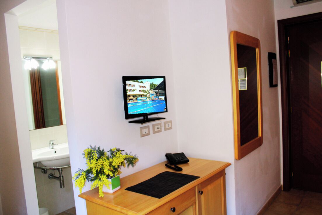 A reception desk with a television displaying a pool view, a telephone, and a vase with yellow flowers.