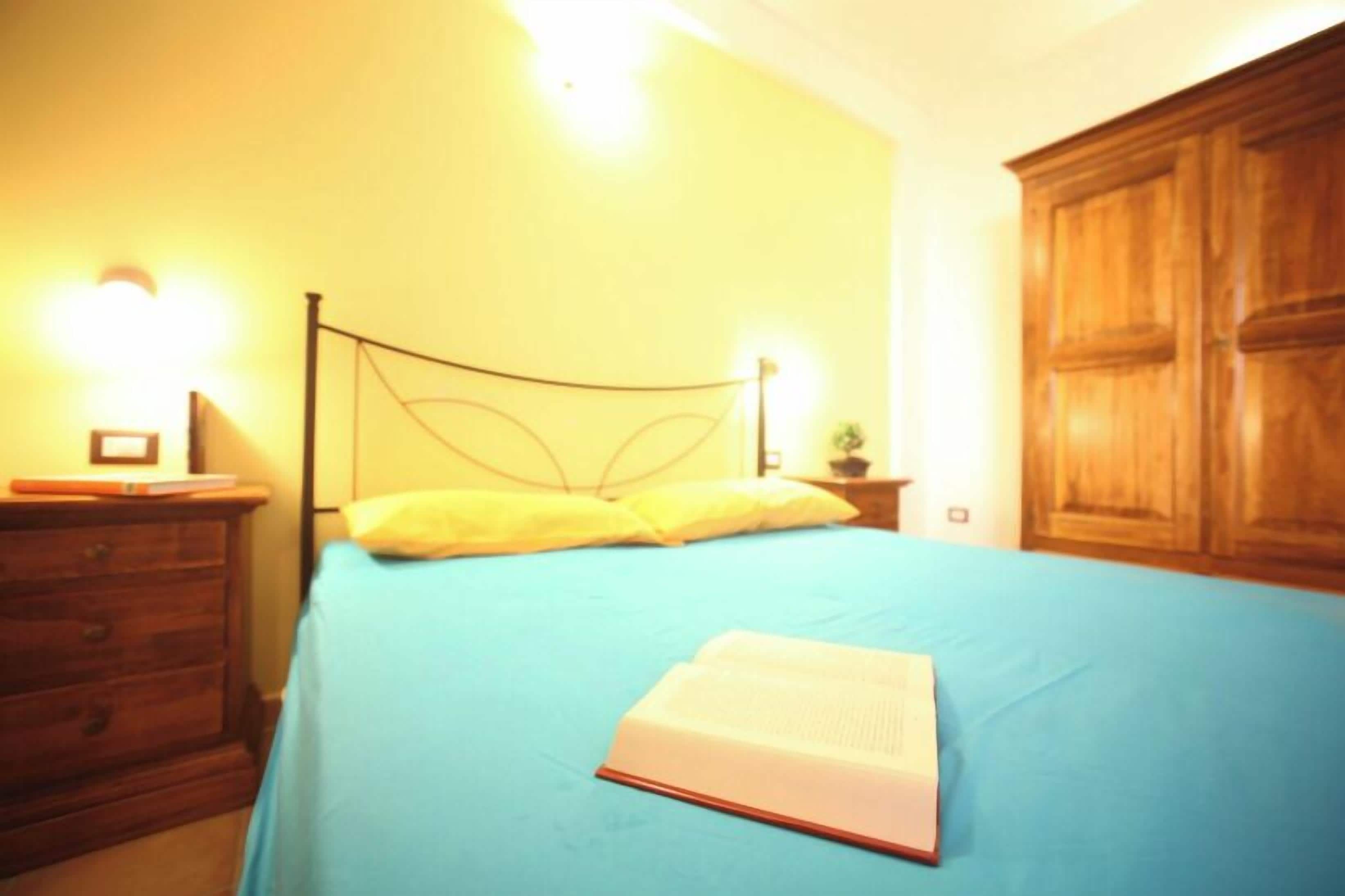 A bed with a blue bedspread, a wooden nightstand with a lamp, and a wooden wardrobe.