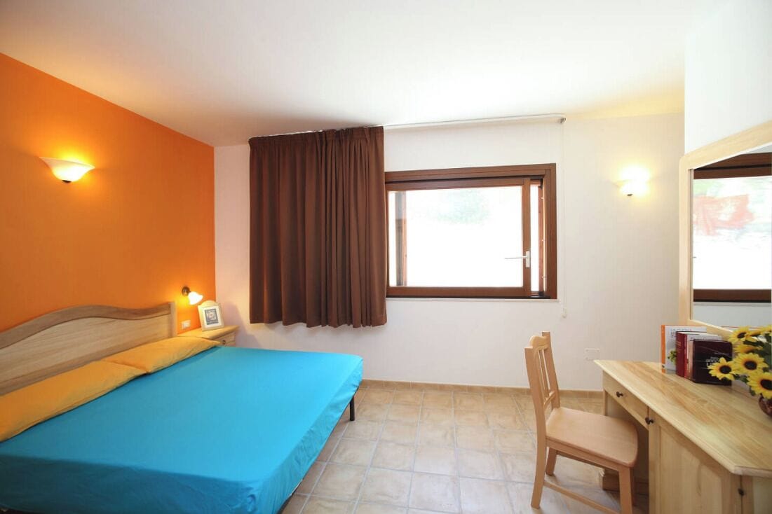 Une chambre à coucher comprenant un lit, un bureau, une chaise, une fenêtre avec des rideaux et des lampes fixées au mur.