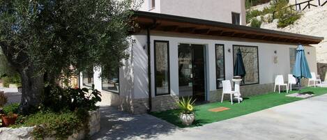 A modern building with a patio area featuring white chairs and a blue umbrella.