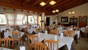 A dining area with multiple tables and chairs, wooden beams on the ceiling, and a large window with curtains.