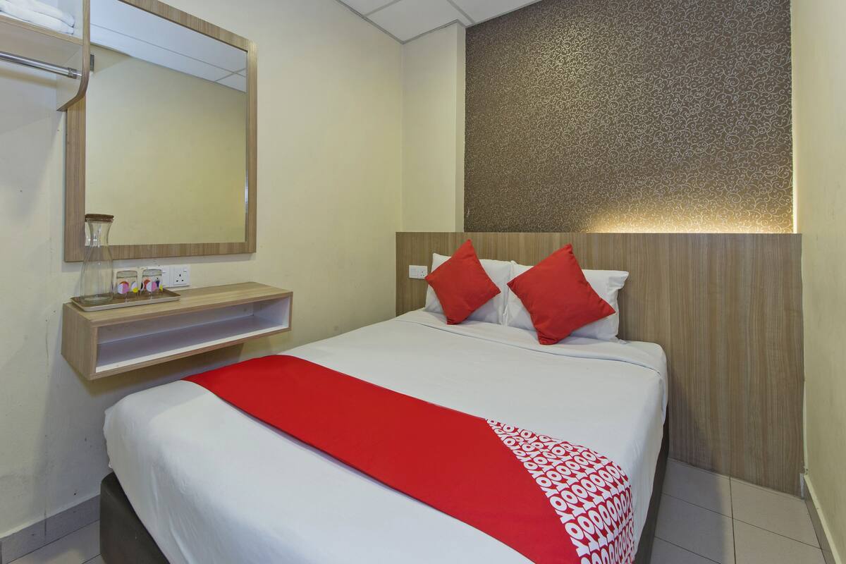 Una habitación de hotel con una cama grande, una mesita de noche con espejo y un panel decorativo en la pared.
