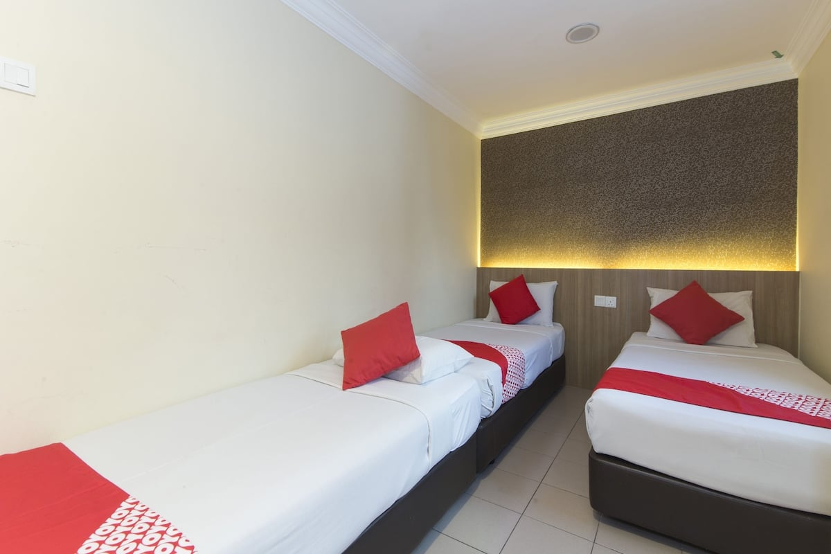 Habitación de hotel con dos camas individuales, cada una con ropa de cama blanca y detalles rojos, cabeceros de madera y una pared texturizada sobre las camas.