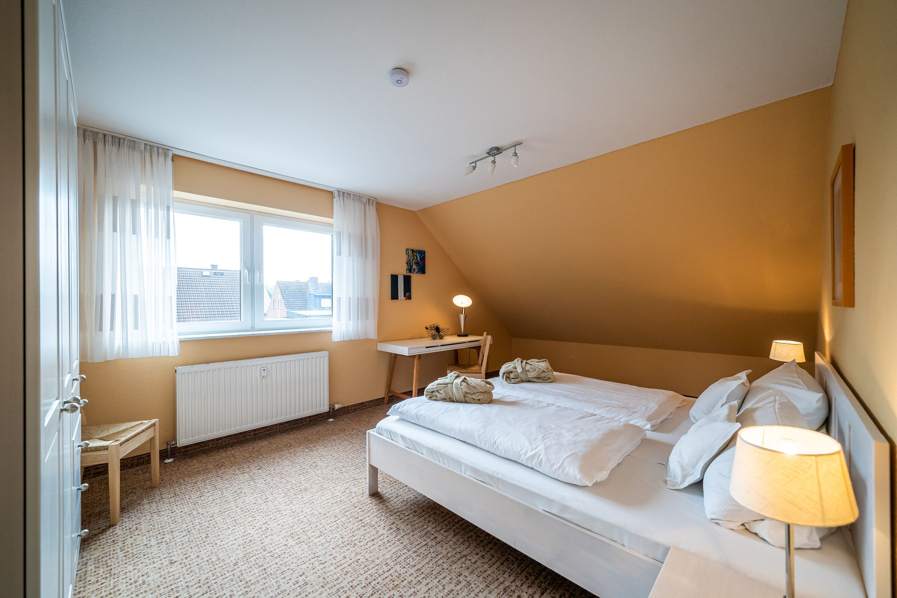 A bedroom with a bed, bedside table, lamp, and a view of the city through a window.