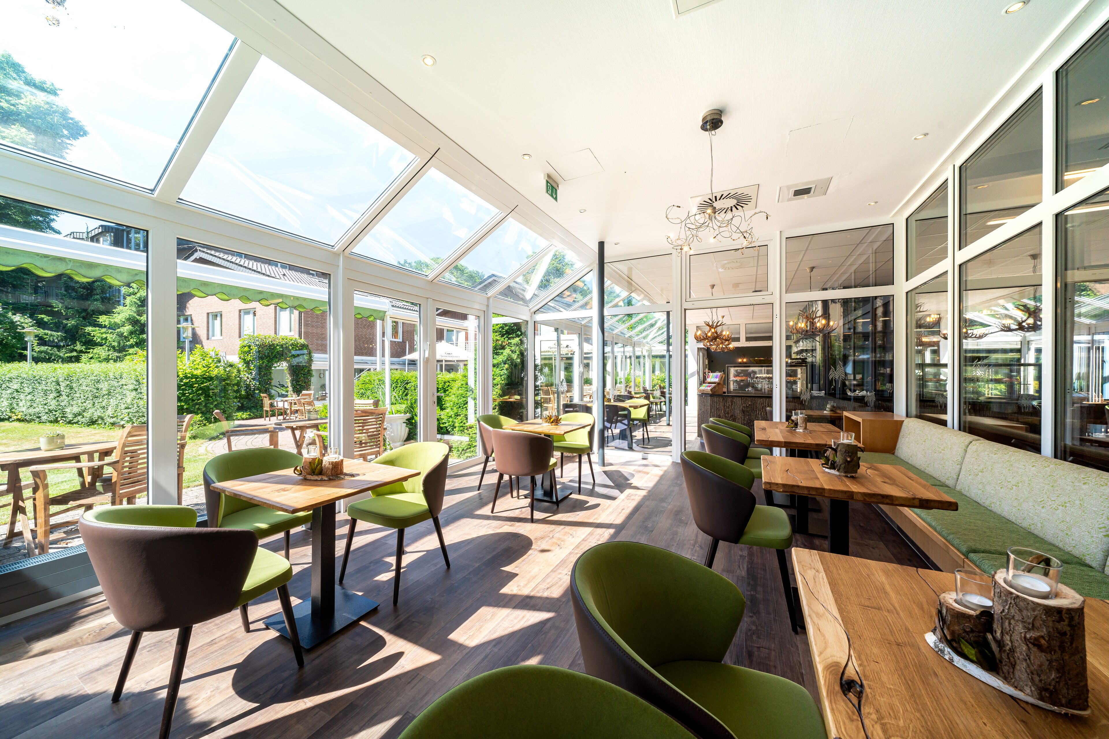 A spacious indoor area with large windows, wooden tables, and green chairs.