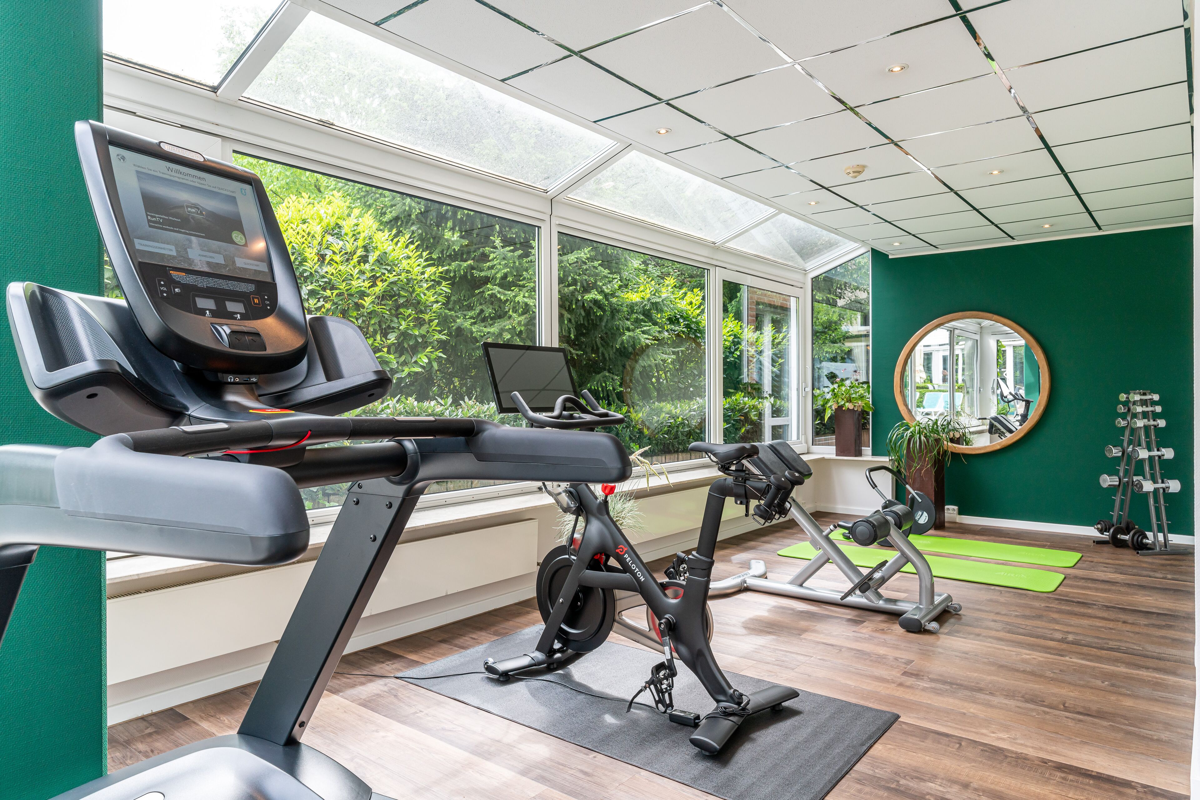 A modern gym with exercise equipment, large windows, and a green wall.