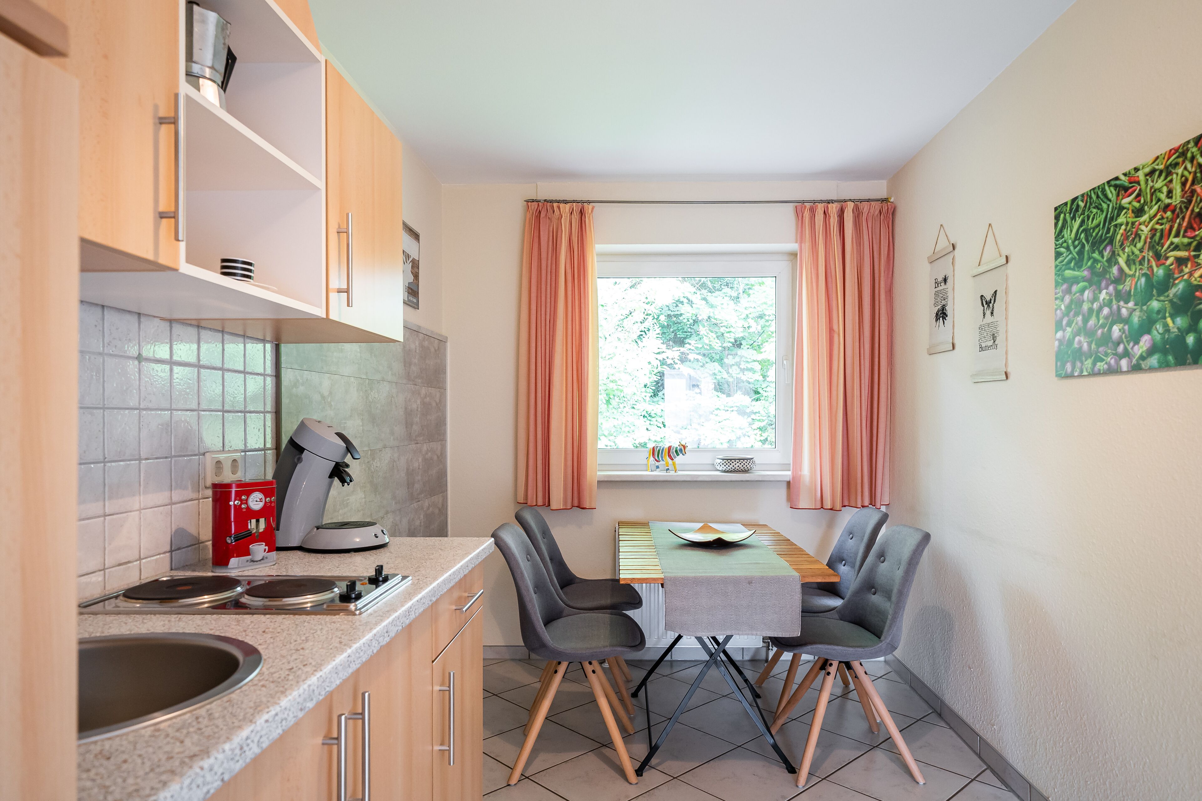 Una cocina compacta con cafetera, un lavamanos y una ventana con cortinas.