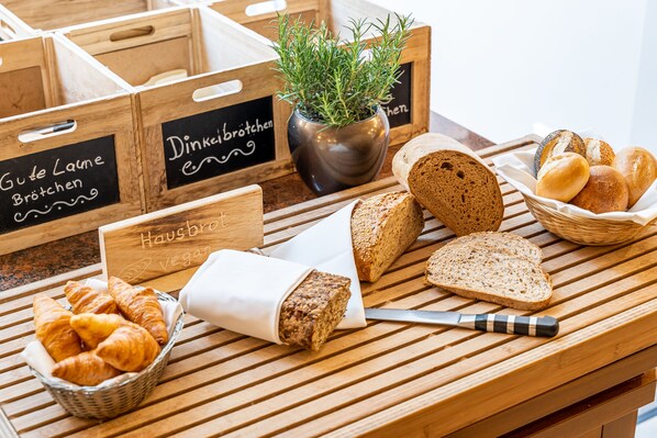 Una mesa de madera con panes variados, un cuchillo y una cesta de cruasanes.