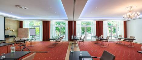A conference room with tables and chairs, large windows, and a chandelier.