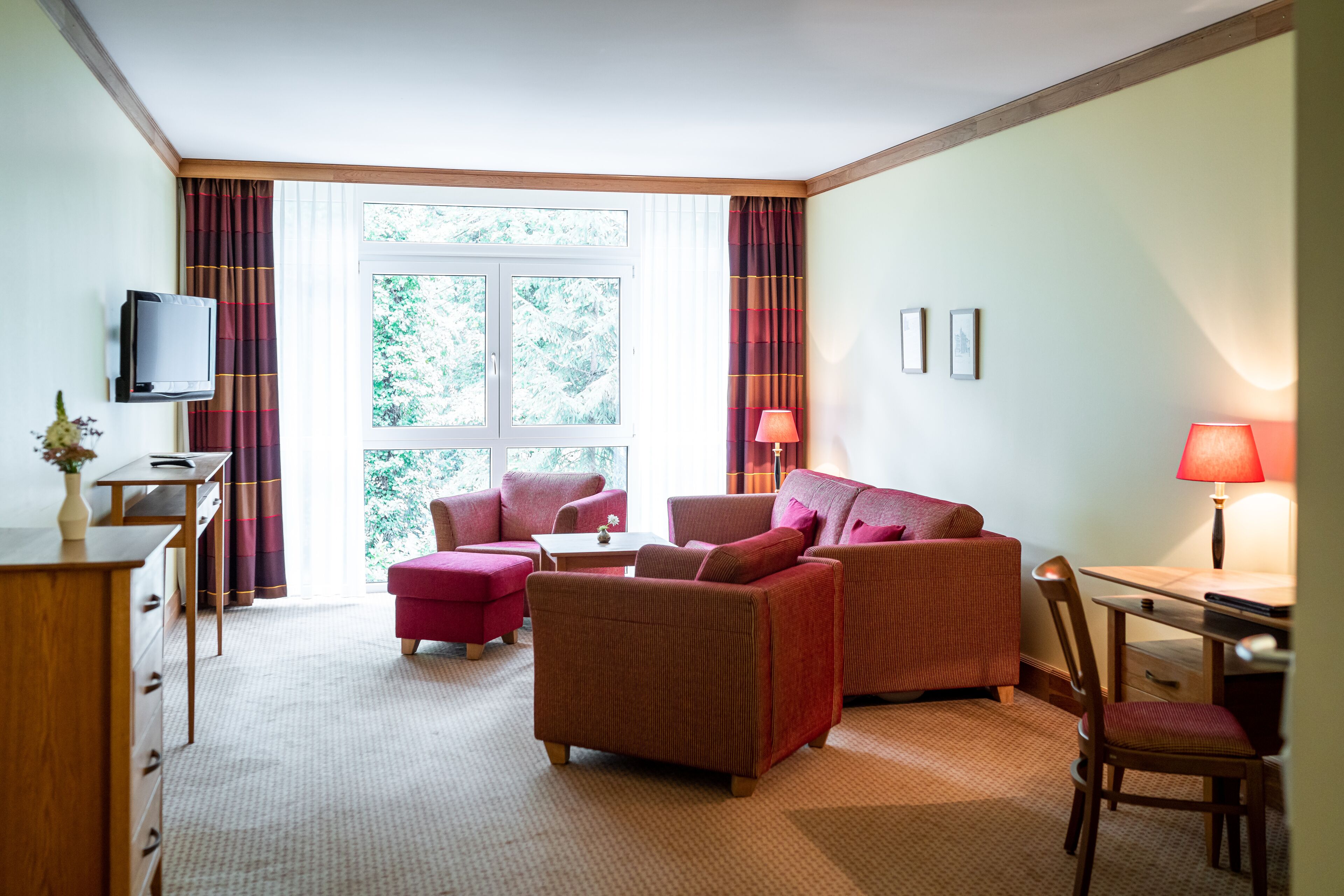A hotel room with a sofa, armchair, and a small table with a lamp.