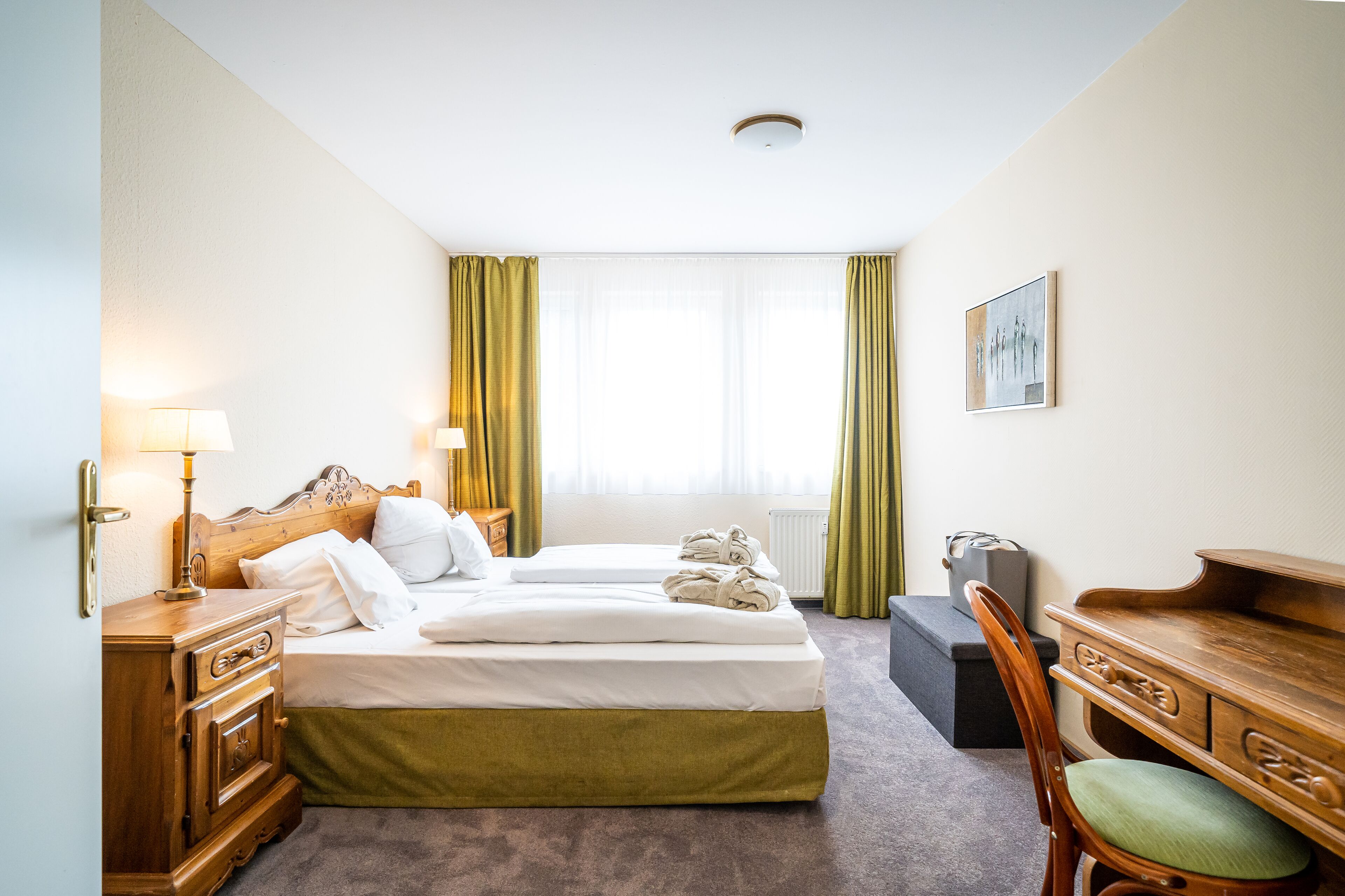 Ein Hotelzimmer mit Doppelbett, einem hölzernen Schminktisch, einem Schreibtisch, einem Stuhl und einem fenster mit Vorhängen.