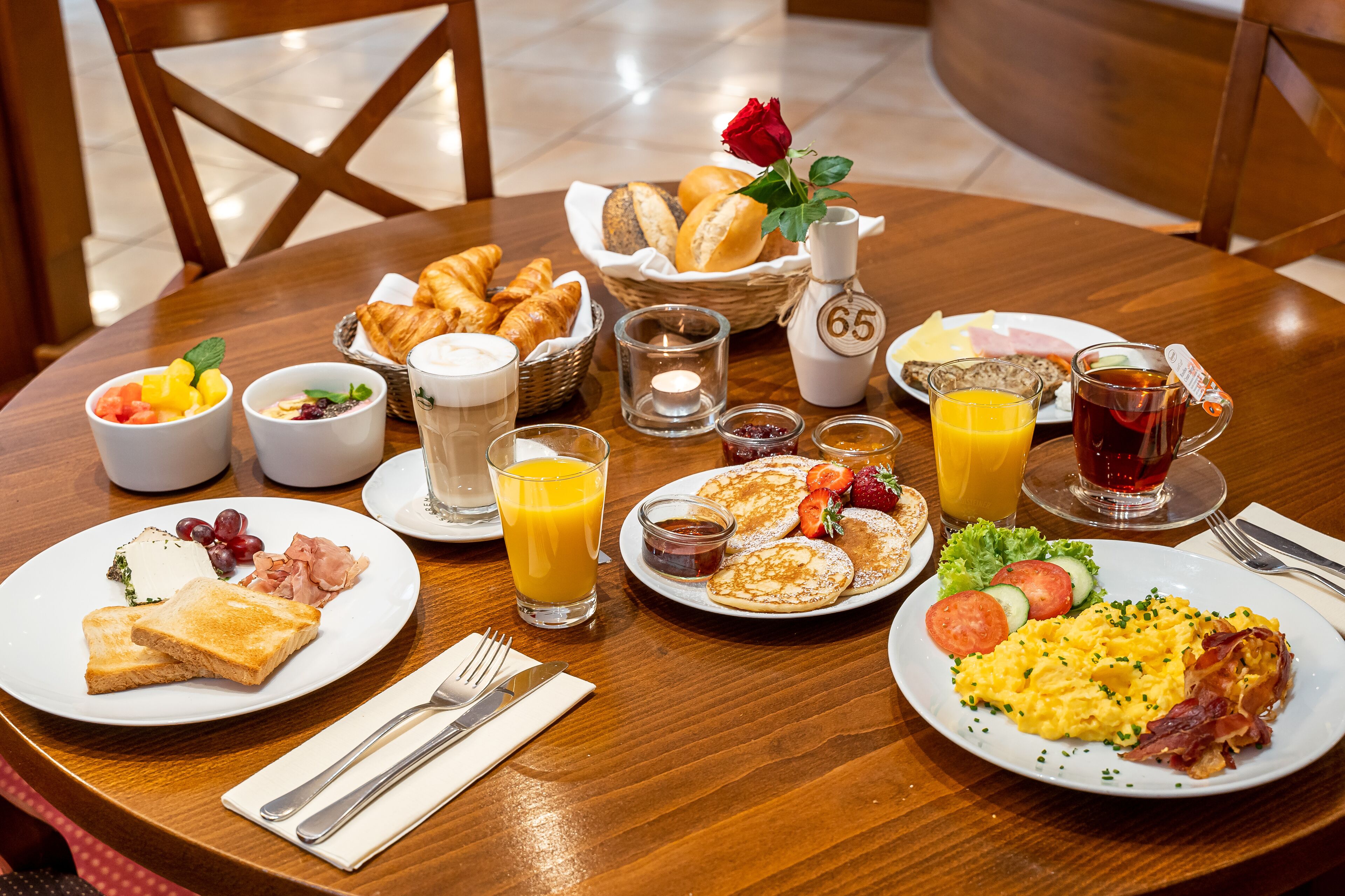 A breakfast setting with croissants, toast, eggs, and juice on a wooden table.