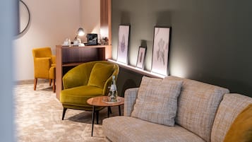 A modern living room with a sofa, a yellow armchair, a small wooden table with a bottle, and framed botanical prints on the wall.