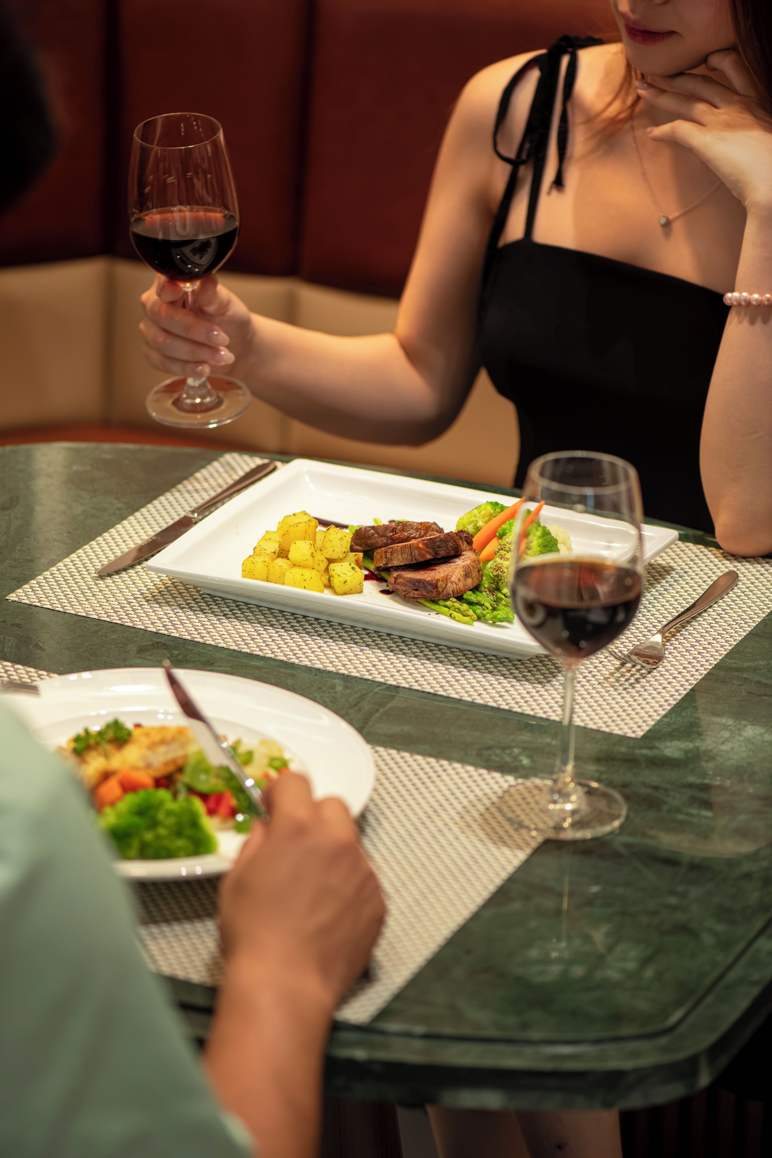 A dining table with plates of food, wine glasses, and cutlery.
