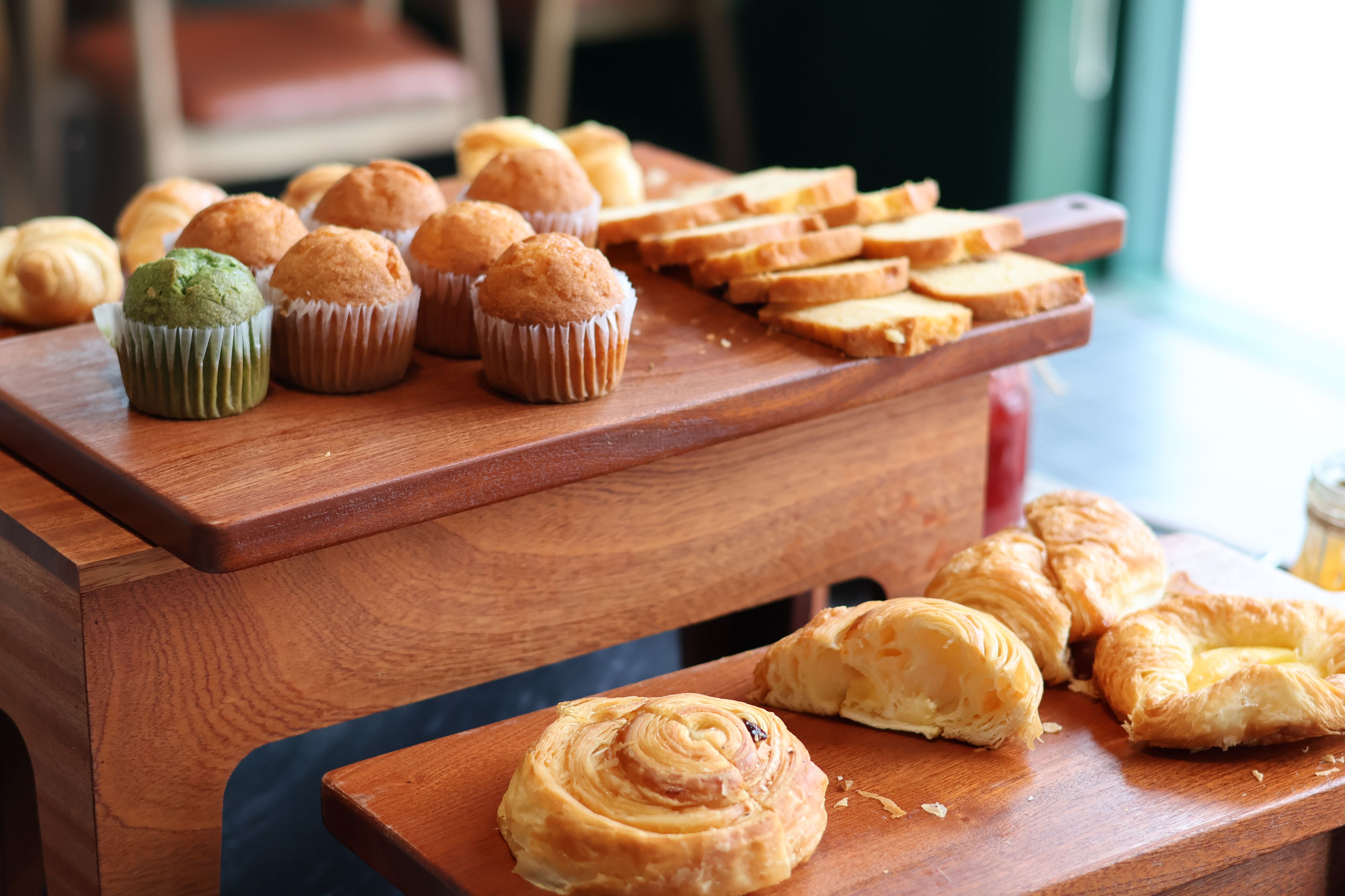 Una mesa de madera con pastelería, incluyendo muffins y croissants.
