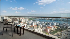 Un balcón con sillas y una mesa, con vistas a un paisaje urbano que incluye edificios y un río.