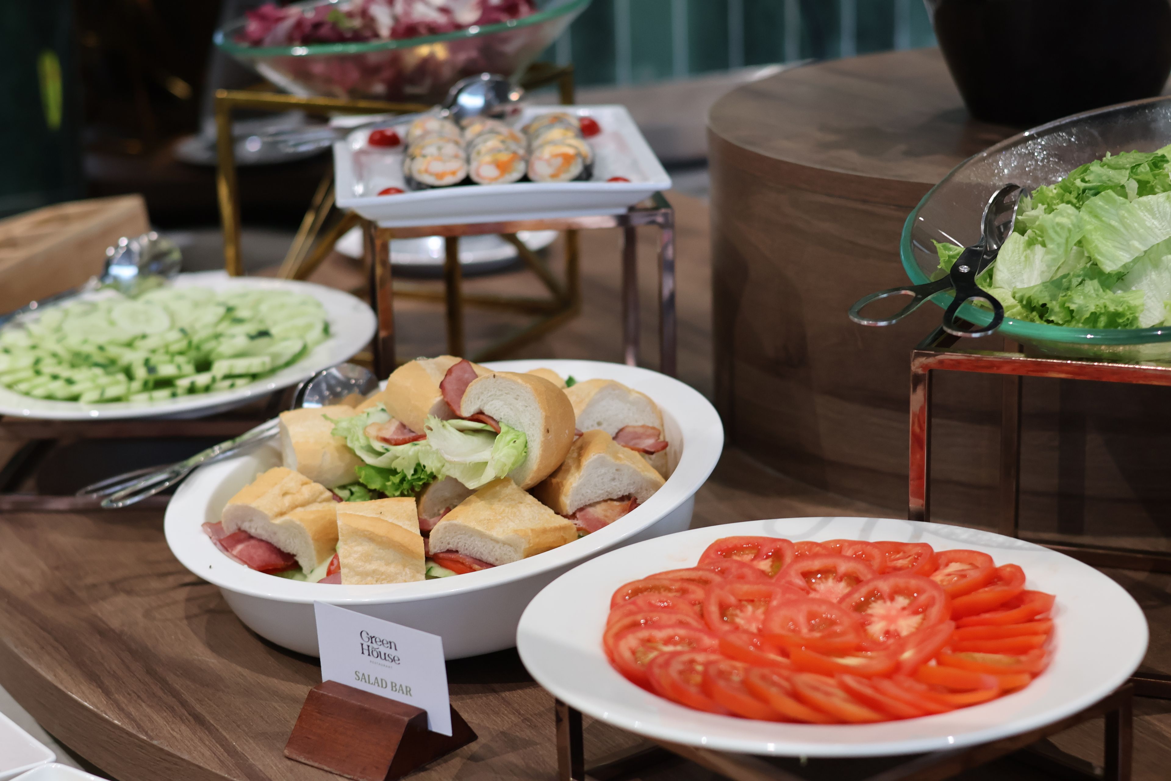 A buffet table with various food items including sandwiches, salads, and sliced tomatoes.