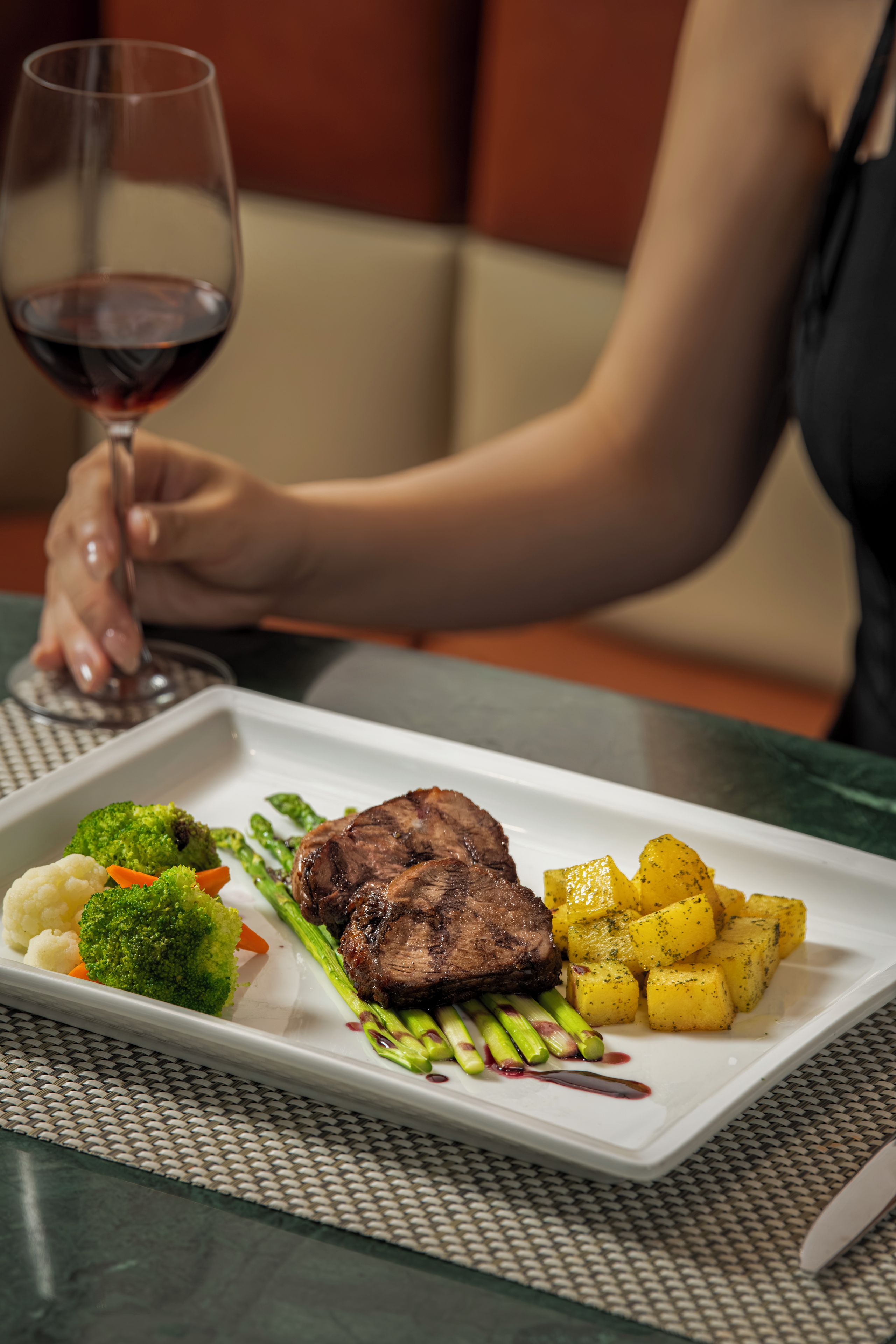 Une table à manger avec une assiette de nourriture, un verre de vin rouge et une personne assise.
