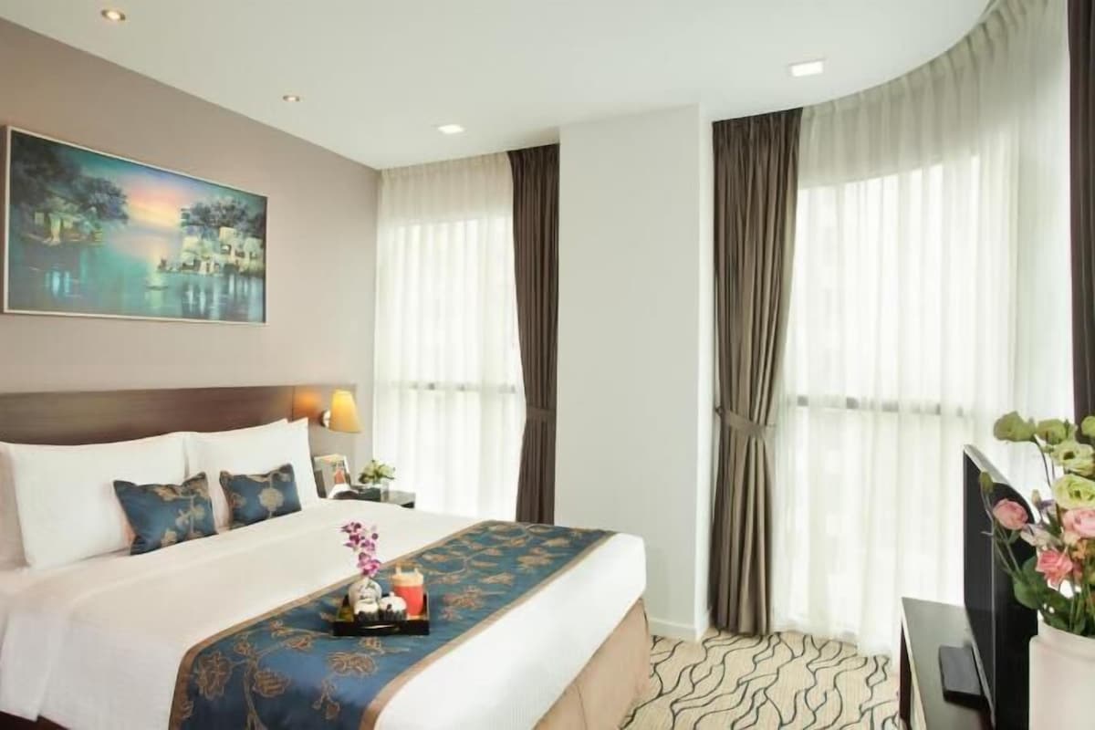 Une chambre d’hôtel avec un lit, un tableau, une table de chevet, un bureau et une fenêtre avec des rideaux.