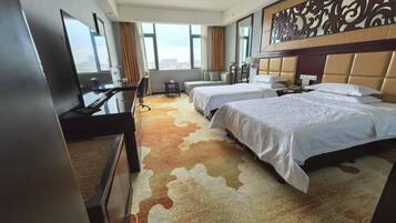 Ein Hotelzimmer mit zwei Betten, einem Schreibtisch, einem Fernseher und Blick auf die Stadt.