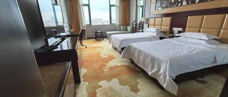 A hotel room with two beds, a desk, a TV, and a view of the city.
