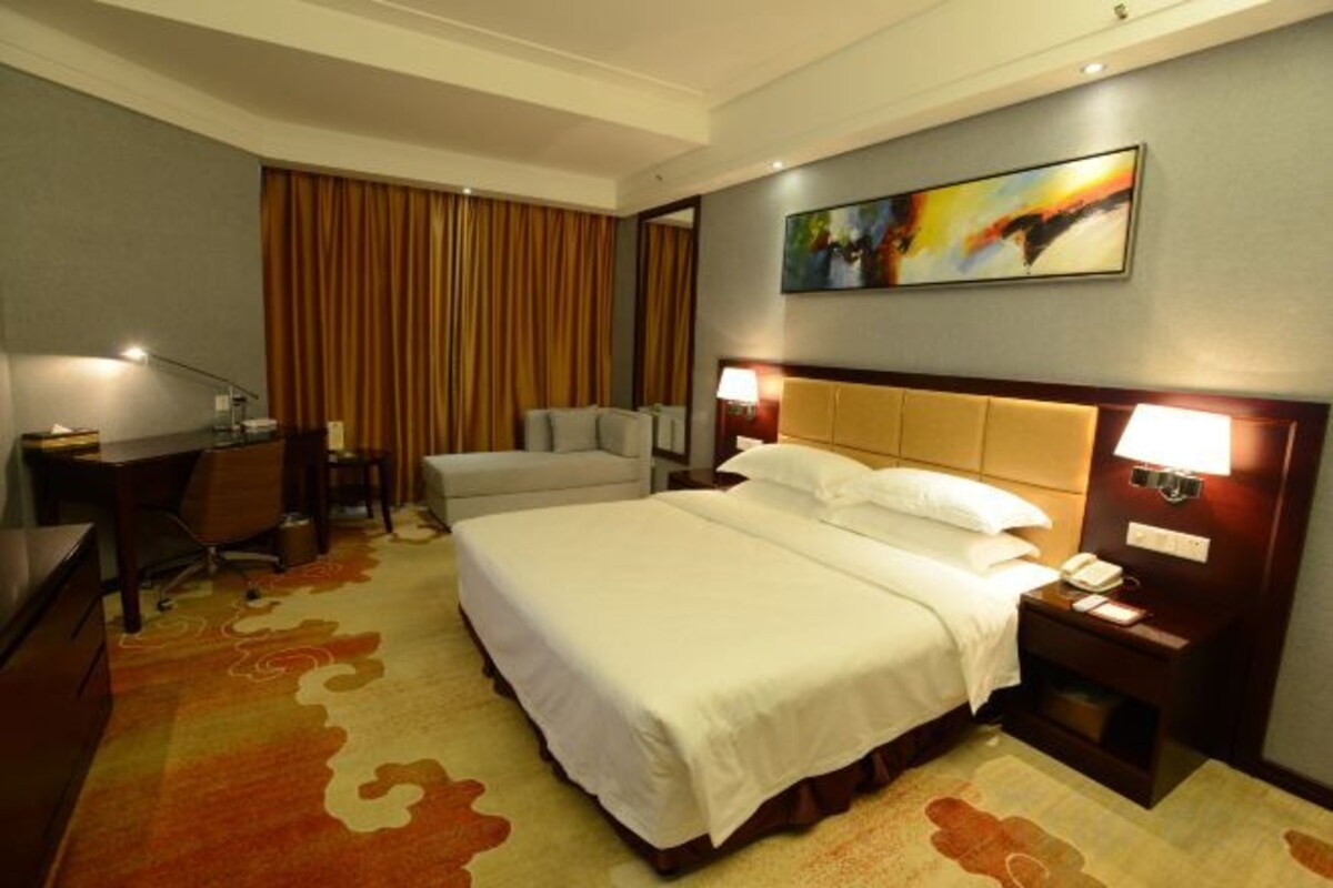 A hotel room with a large bed, a desk, a chair, a nightstand, and a painting on the wall.