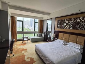 A hotel room with a large bed, a sofa, a desk, and a view of the city. - Manhattan International Hotel (Huaibei)