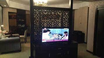Ein Wohnzimmer mit einem Flachbildfernseher auf einem Schrank, einer Couch, einer Wandverkleidung und einer Deckenleuchte.