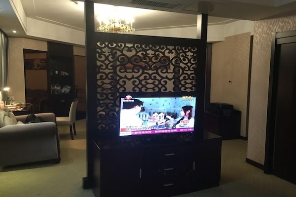 A living room with a flat-screen TV on a stand, a sofa, a decorative wall panel, and a chandelier. - Manhattan International Hotel (Huaibei)