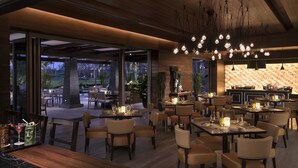 Un restaurante moderno con una combinación de mesas dentro y fuera, que presenta una pared de piedra y lámparas colgantes.