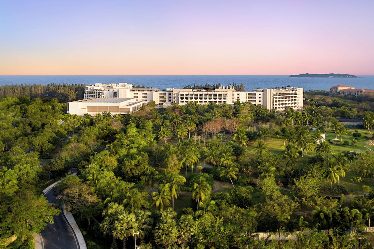 A resort with multiple buildings, lush greenery, and a view of the ocean.
