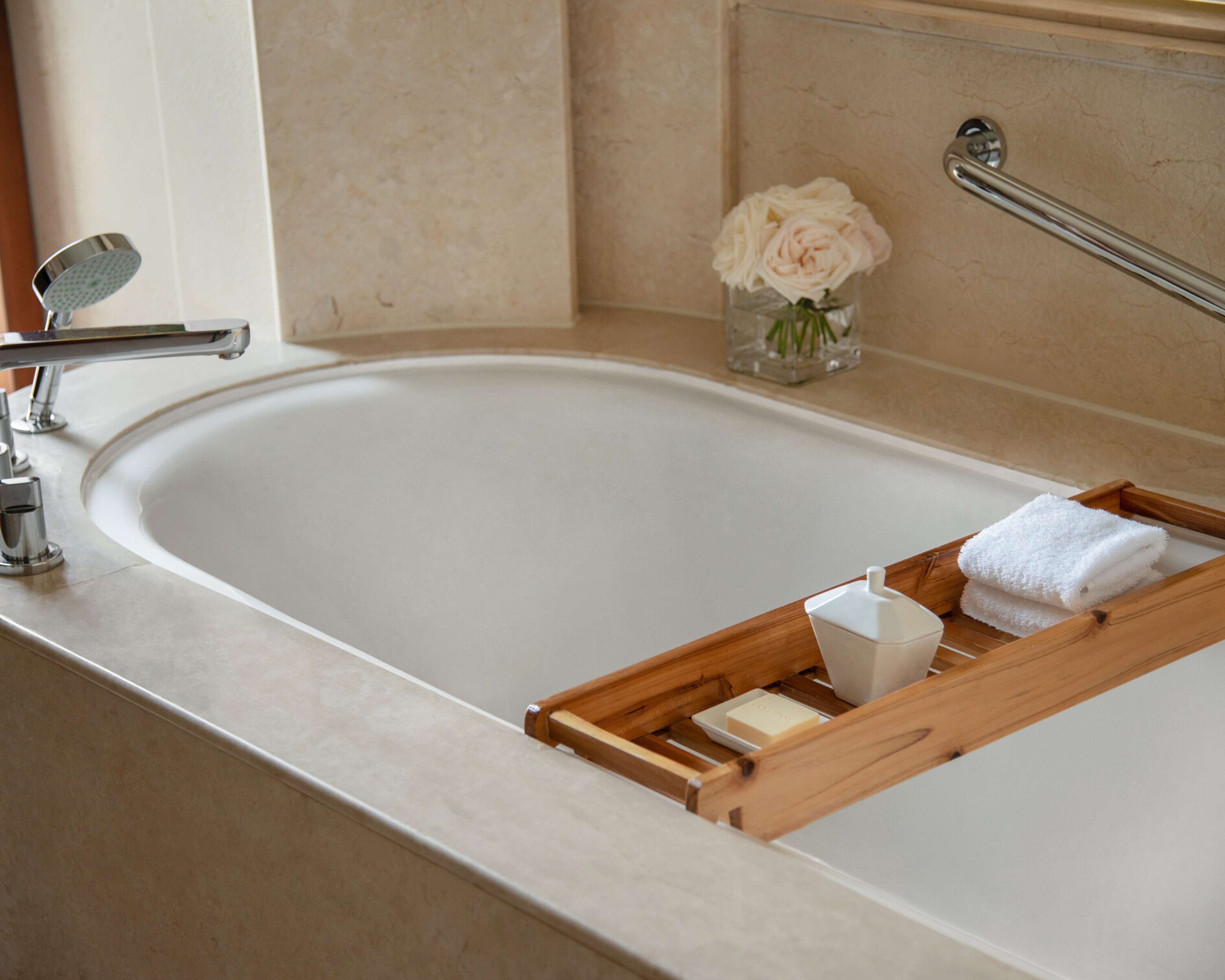 A bathroom with a bathtub, a glass of water, a white rose, and a wooden tray with a bar of soap.