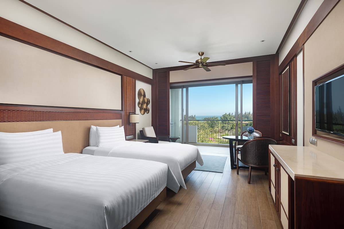 A hotel room with two beds, a balcony with a view, a ceiling fan, and a television.