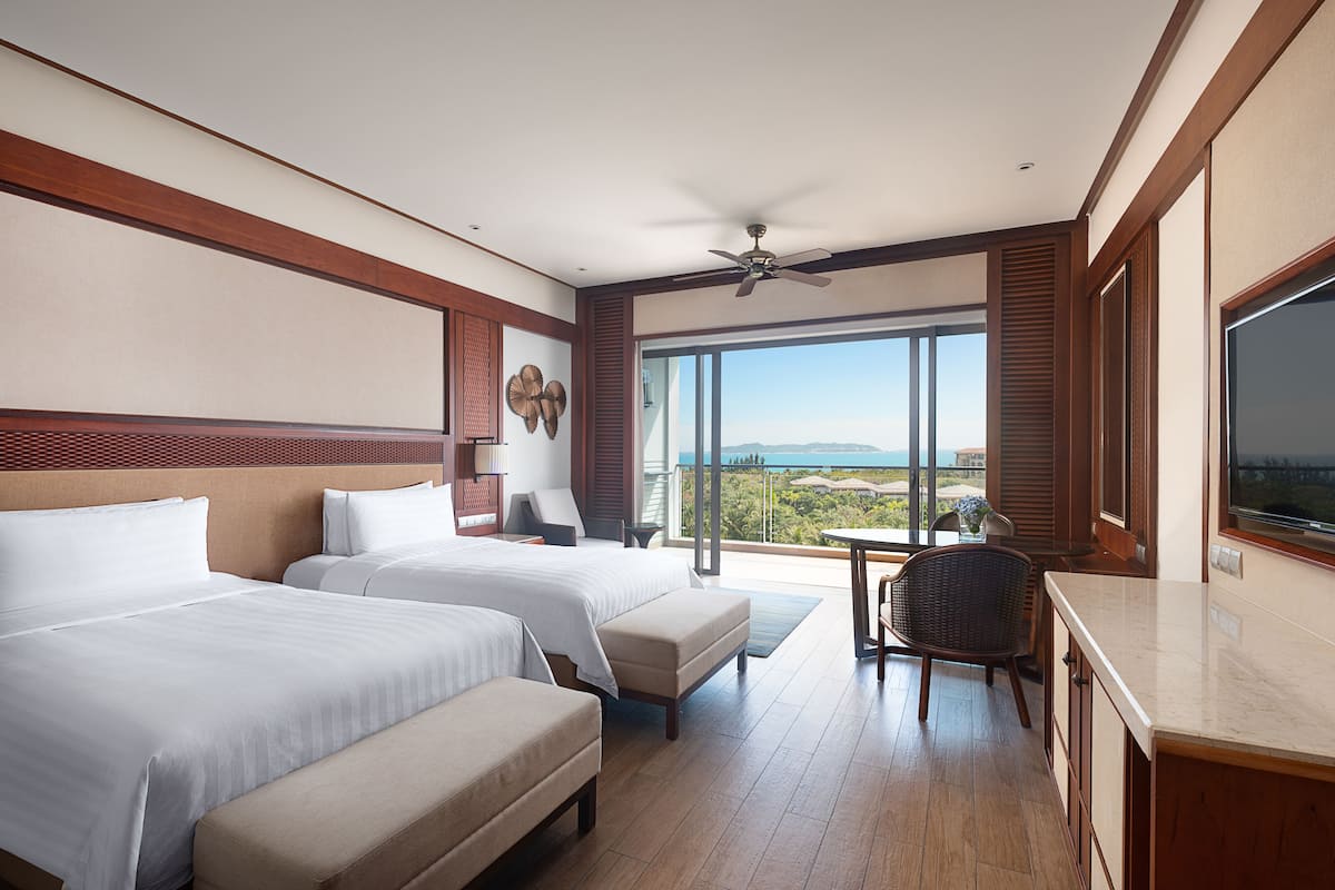 A hotel room with two beds, a balcony, a television, and a view of the ocean.