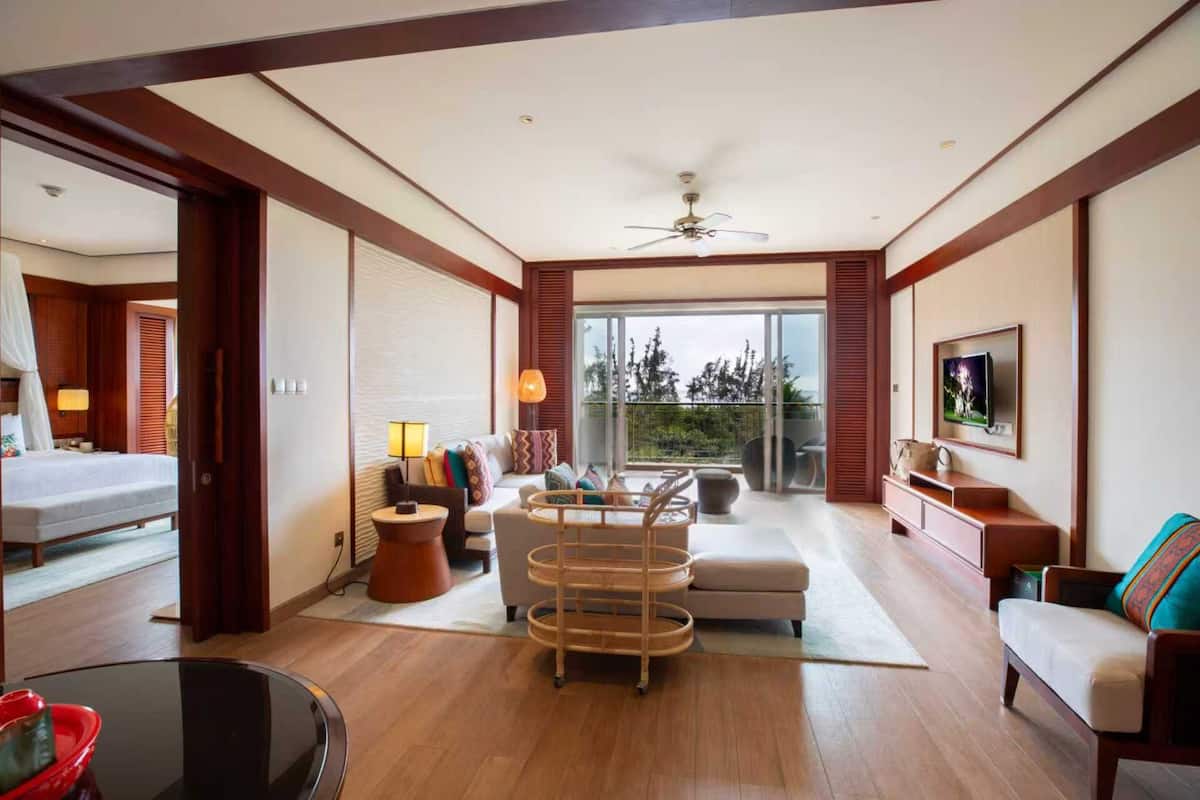 A spacious living area with a sofa, a coffee table, a TV, and a balcony with a view of trees.