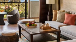 Una sala de estar moderna con un balcón que ofrece vistas panorámicas, una silla de mimbre, un sofá con cojines y una mesa de centro con fruta y un calentador de agua.