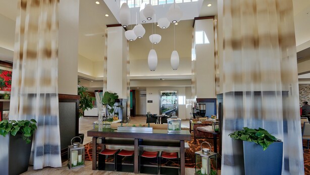Un hall d’entrée spacieux avec un plafond haut, de nombreuses suspensions et un espace salon central agrémenté d’une machine à café.