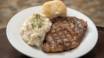 Une assiette comprenant un steak grillé, de la purée de pommes de terre et un petit pain.
